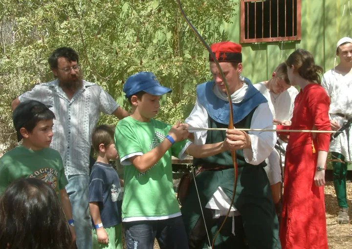 מדריך מסייע לילדים להתנסות בקליעה בחץ וקשת בפסטיבל.