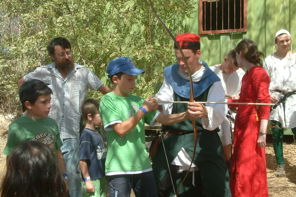 מדריך מסייע לילדים להתנסות בקליעה בחץ וקשת בפסטיבל.