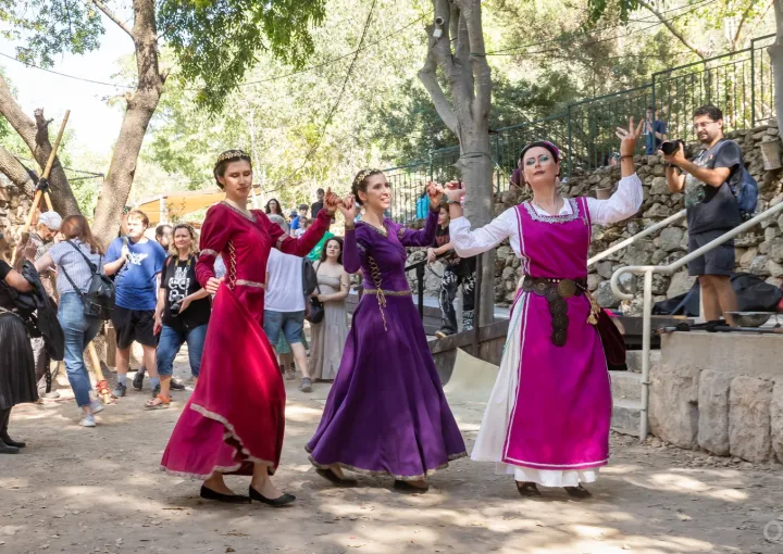 שלוש משתתפות בתלבושות היסטוריות צבעוניות מבצעות ריקוד מימי הביניים.